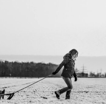 Overcast snowy day with a woman pulling a child in a sled
                  